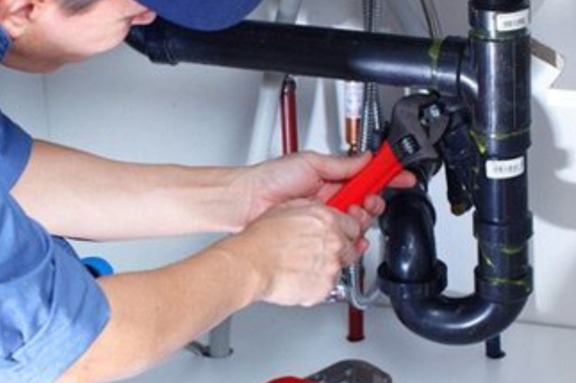 Johnny Jones Plumbing - A man is fixing a pipe with a wrench.