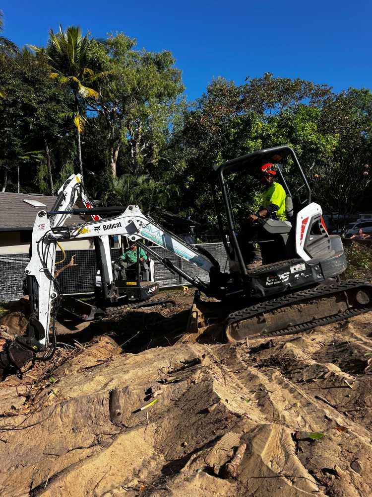A Man is Driving a Small Excavator in a Dirt Field — Advanced Vegetation Management in Bayview Heights, QLD