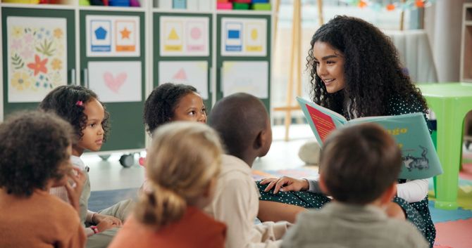 Une enseignante lit un livre coloré à des enfants dans une salle de classe lumineuse ornée d'affiches.