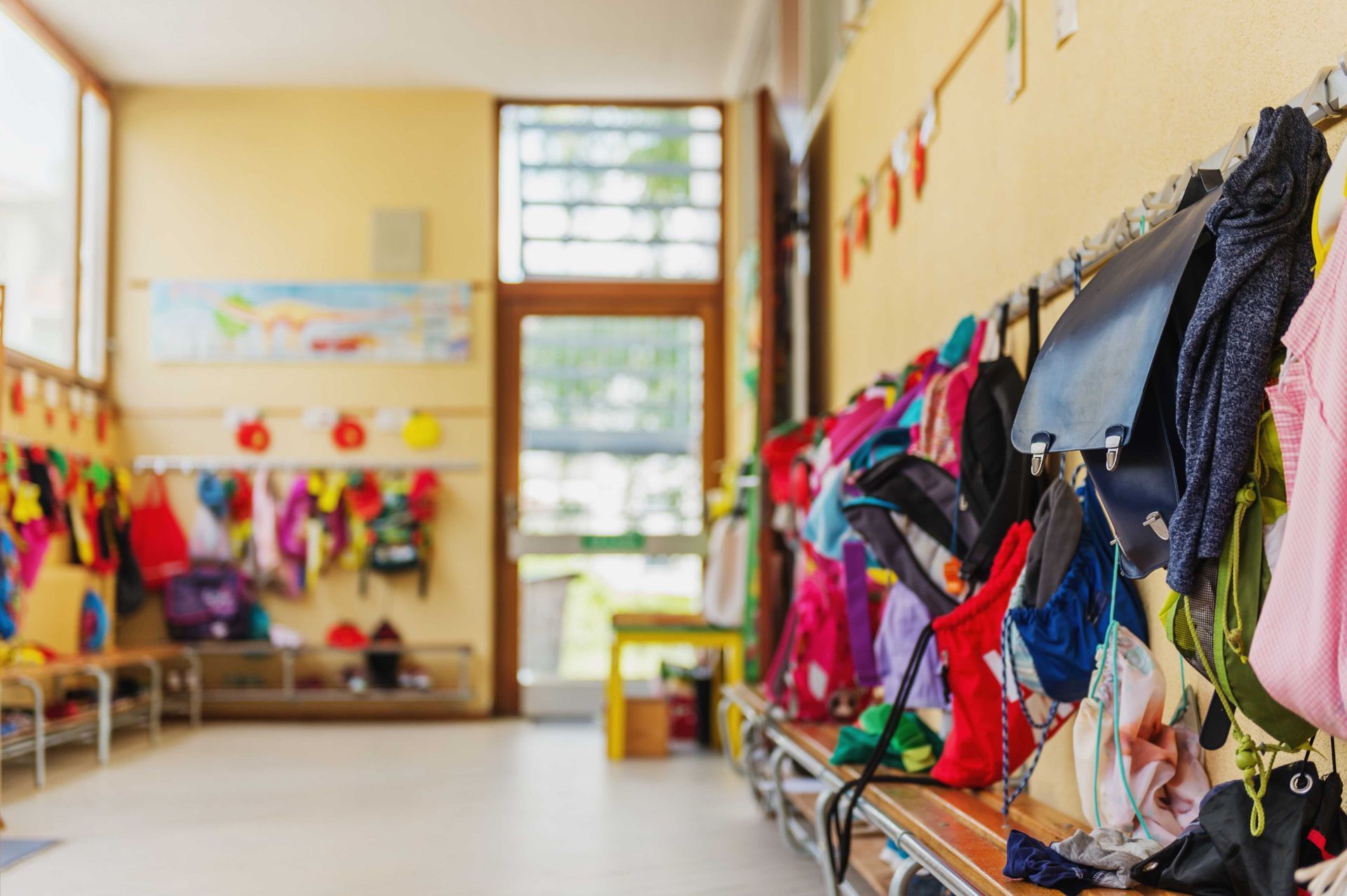 Des sacs à dos et des manteaux colorés suspendus dans un couloir lumineux d'école ou de garderie