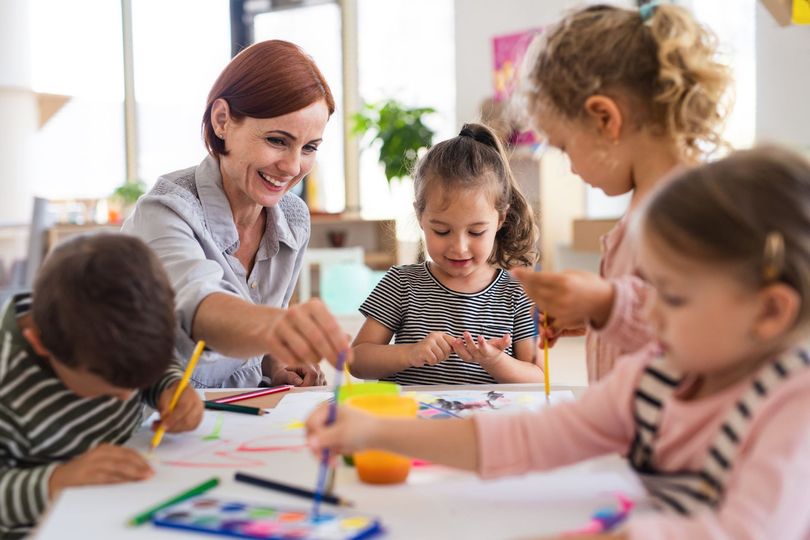 Un enseignant guide des enfants dans une salle de classe pendant qu'ils dessinent avec des crayons de couleur à une table