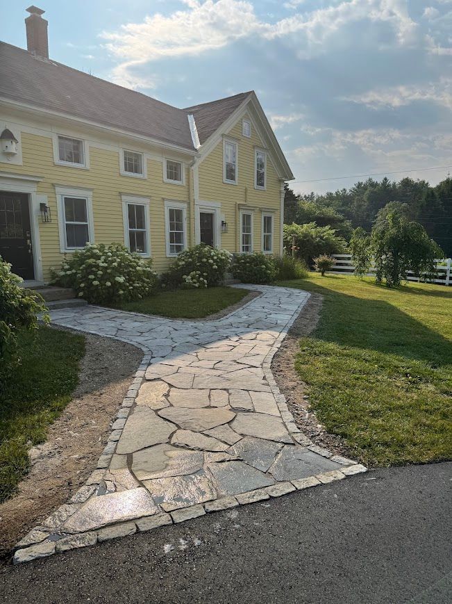 Yellow house with stone pathway and greenery. Sunny day.