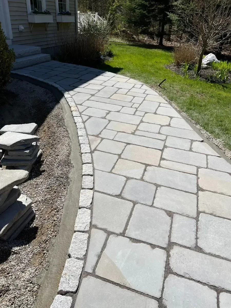 Stone walkway curving towards a house, with green grass and bordering stones.