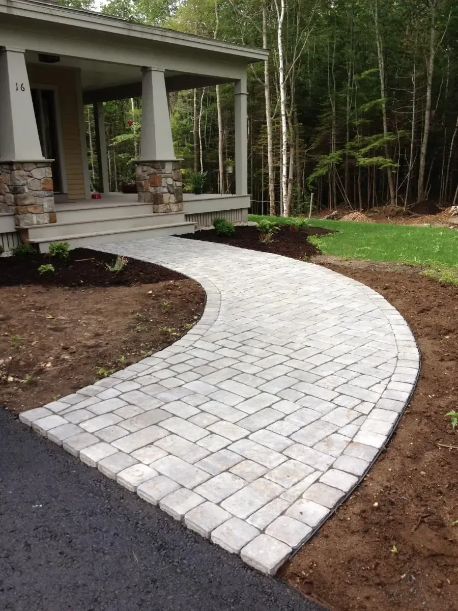 Curving brick paver walkway leading to a house with a porch.