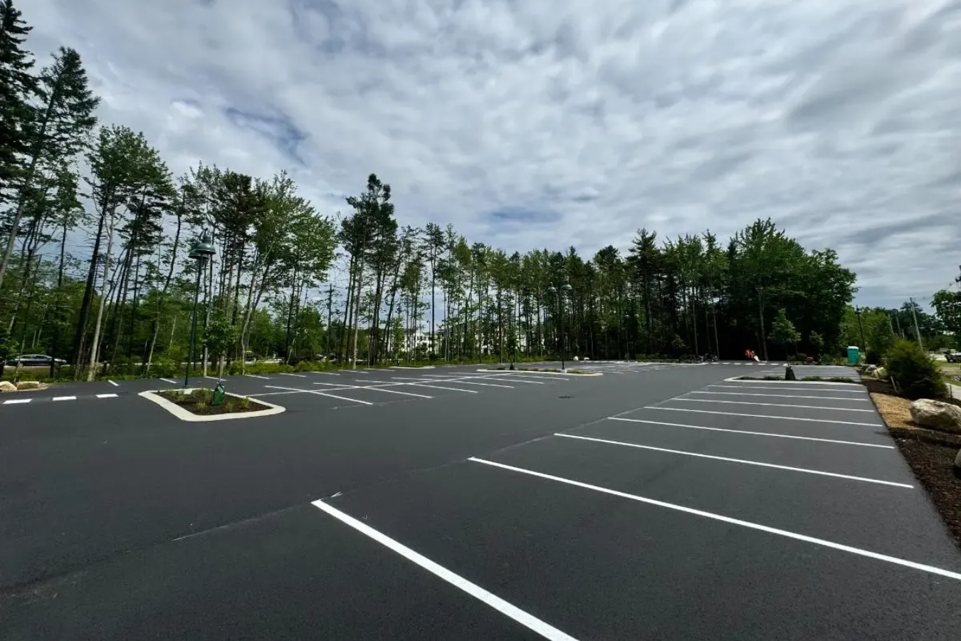 Empty paved parking lot with white lines, trees, and cloudy sky.