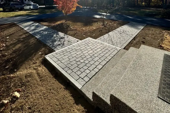 Brick pathways converge at a concrete landing and steps. Brown and gray tones are dominant.
