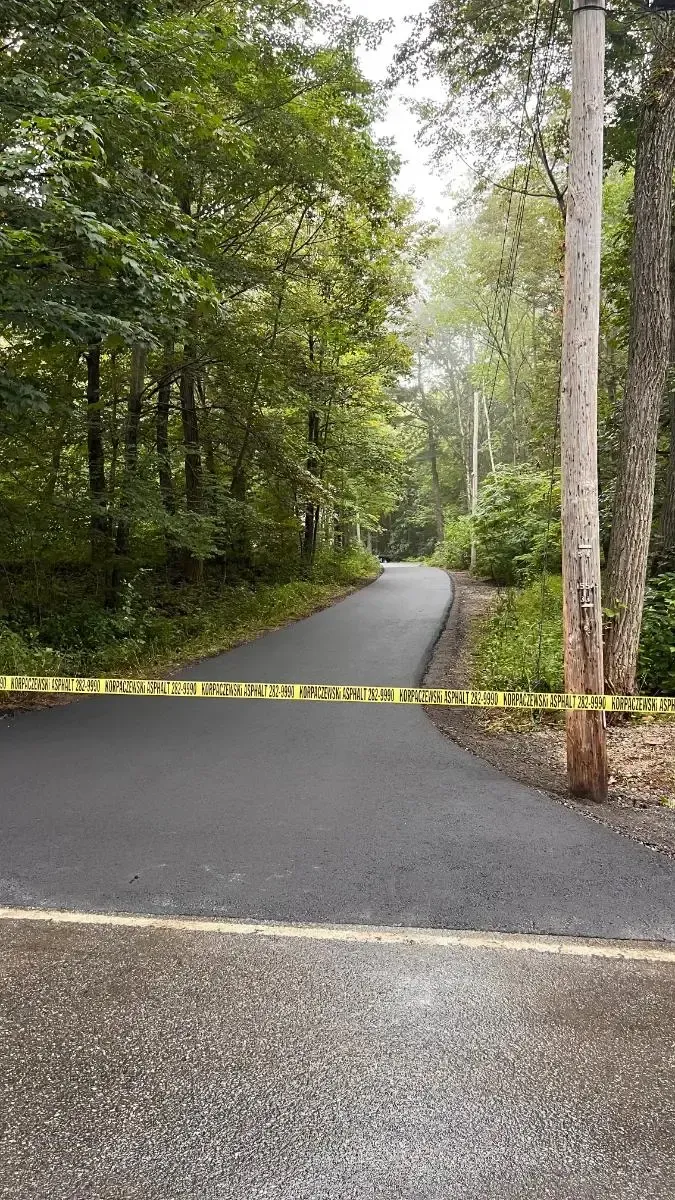 Paved path through trees, blocked by yellow caution tape.