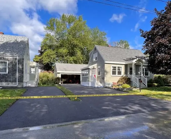 House with teal siding, dark driveway, and green lawn under a blue sky, framed by trees.