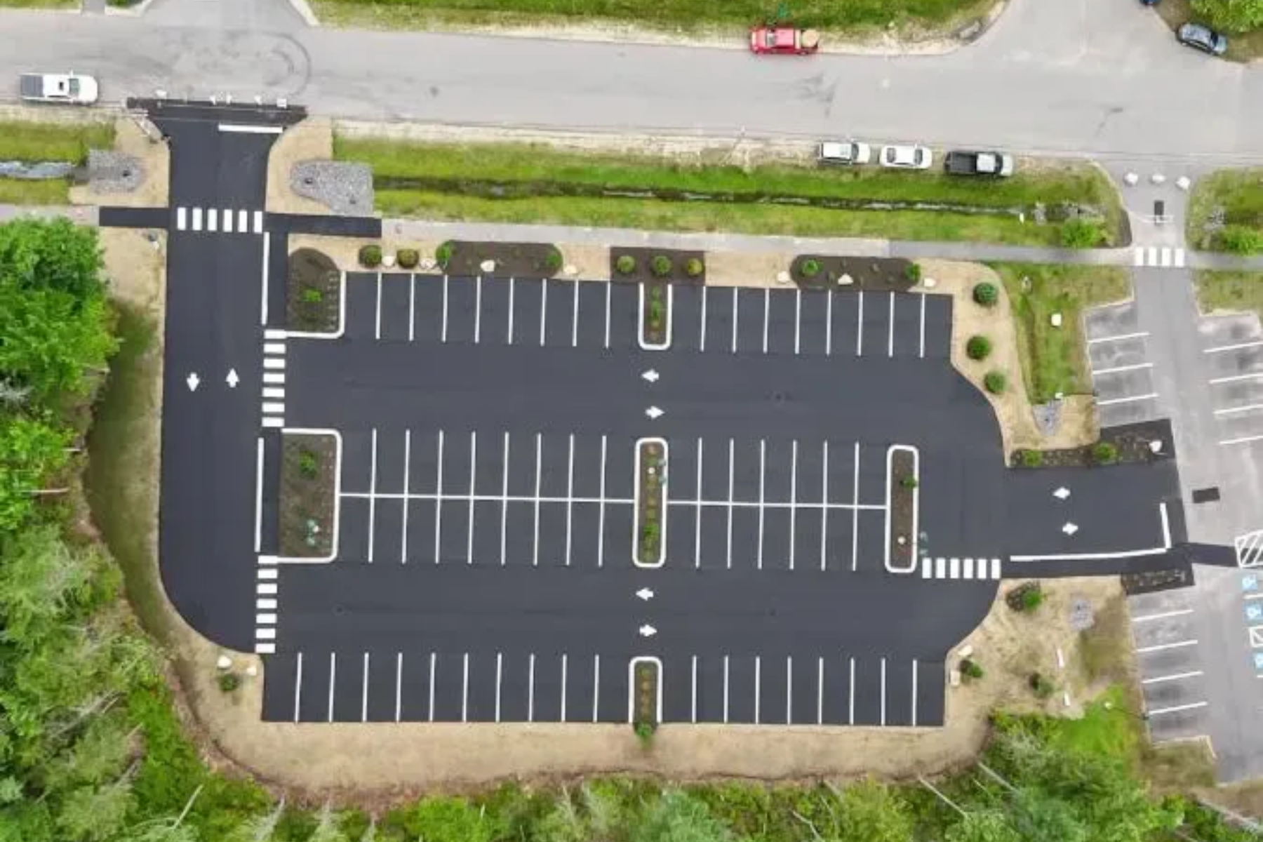 Aerial view of an asphalt parking lot with white parking lines, landscaping, and crosswalks.