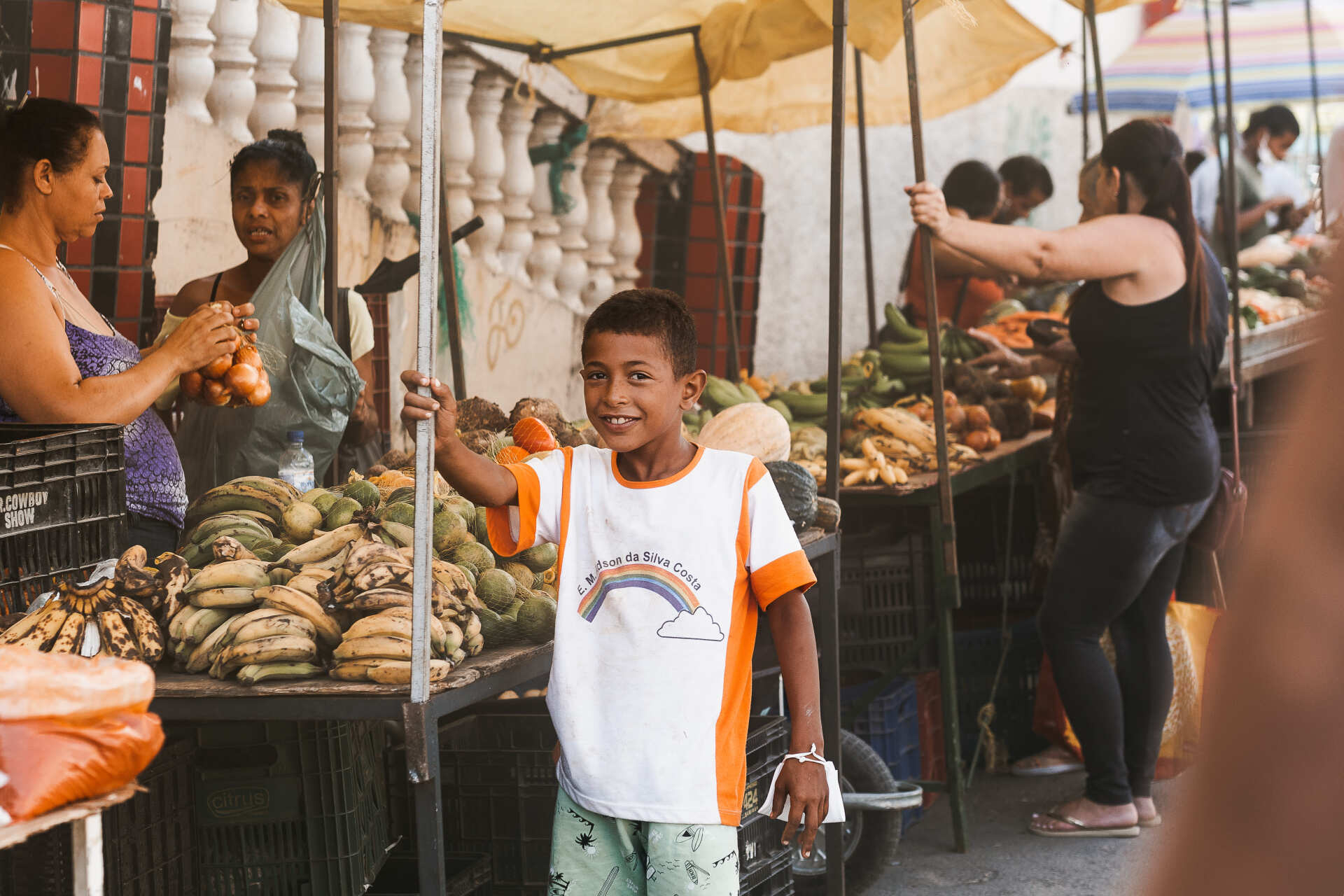 Um menino está parado em frente a uma barraca de frutas em um mercado.