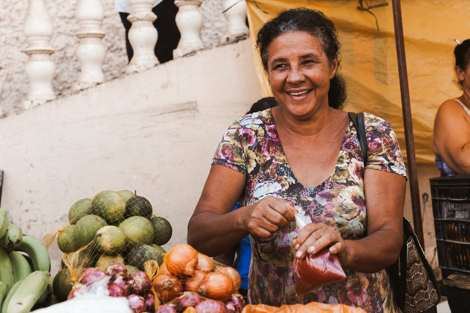 Uma mulher está diante de uma mesa cheia de frutas e legumes.