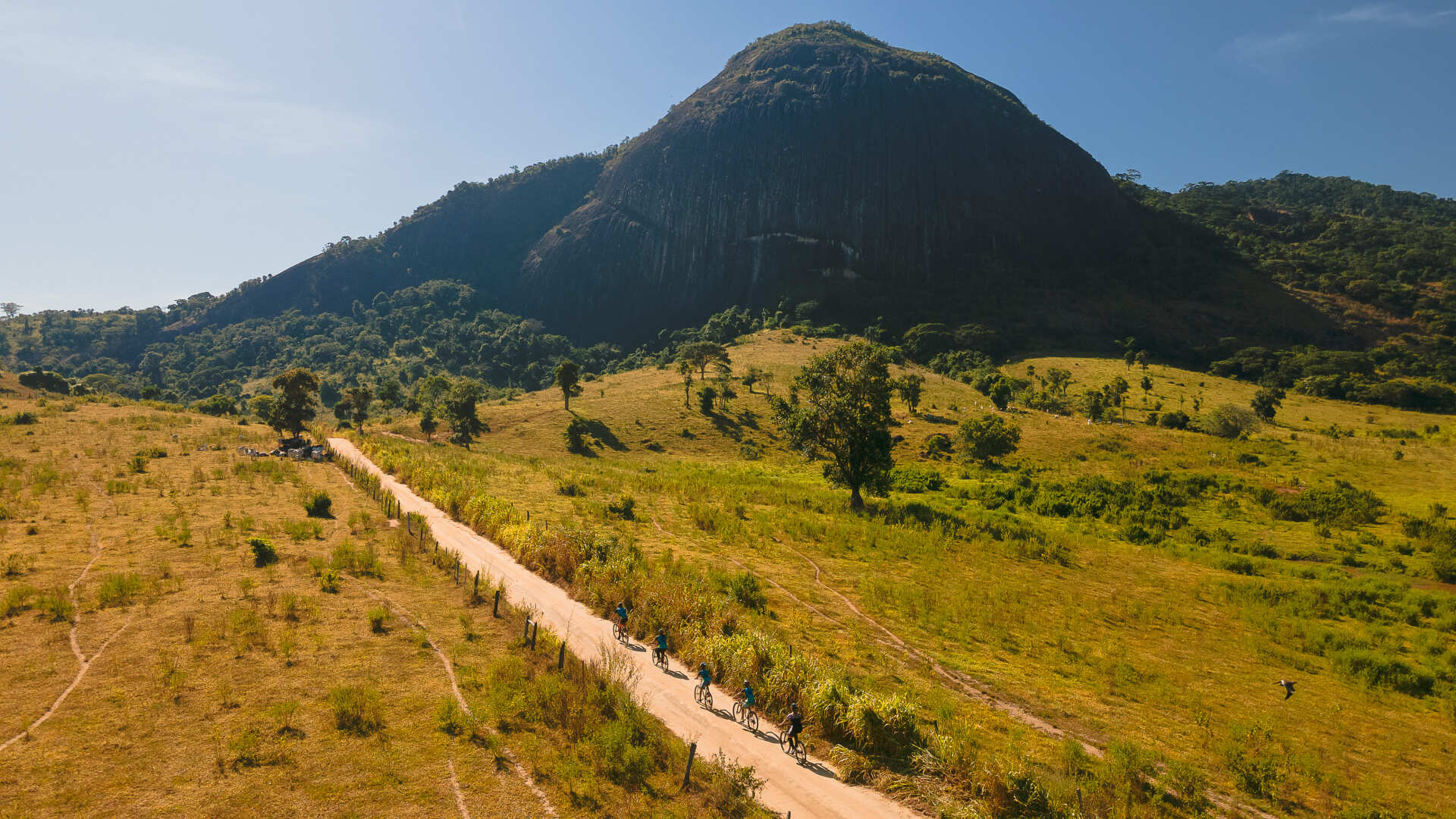 Um grupo de pessoas pedala por uma estrada de terra nas montanhas.