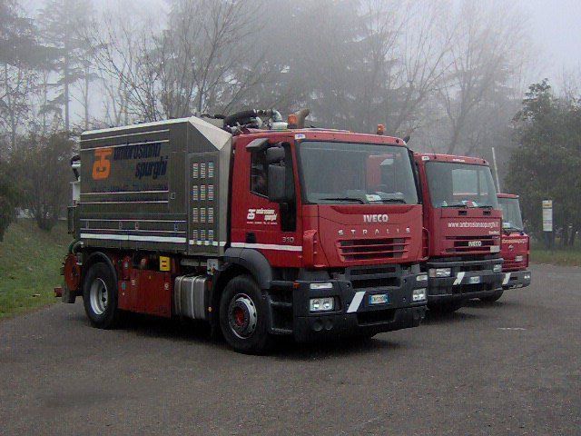Tre camion Iveco rossi parcheggiati all'aperto in una giornata nuvolosa.