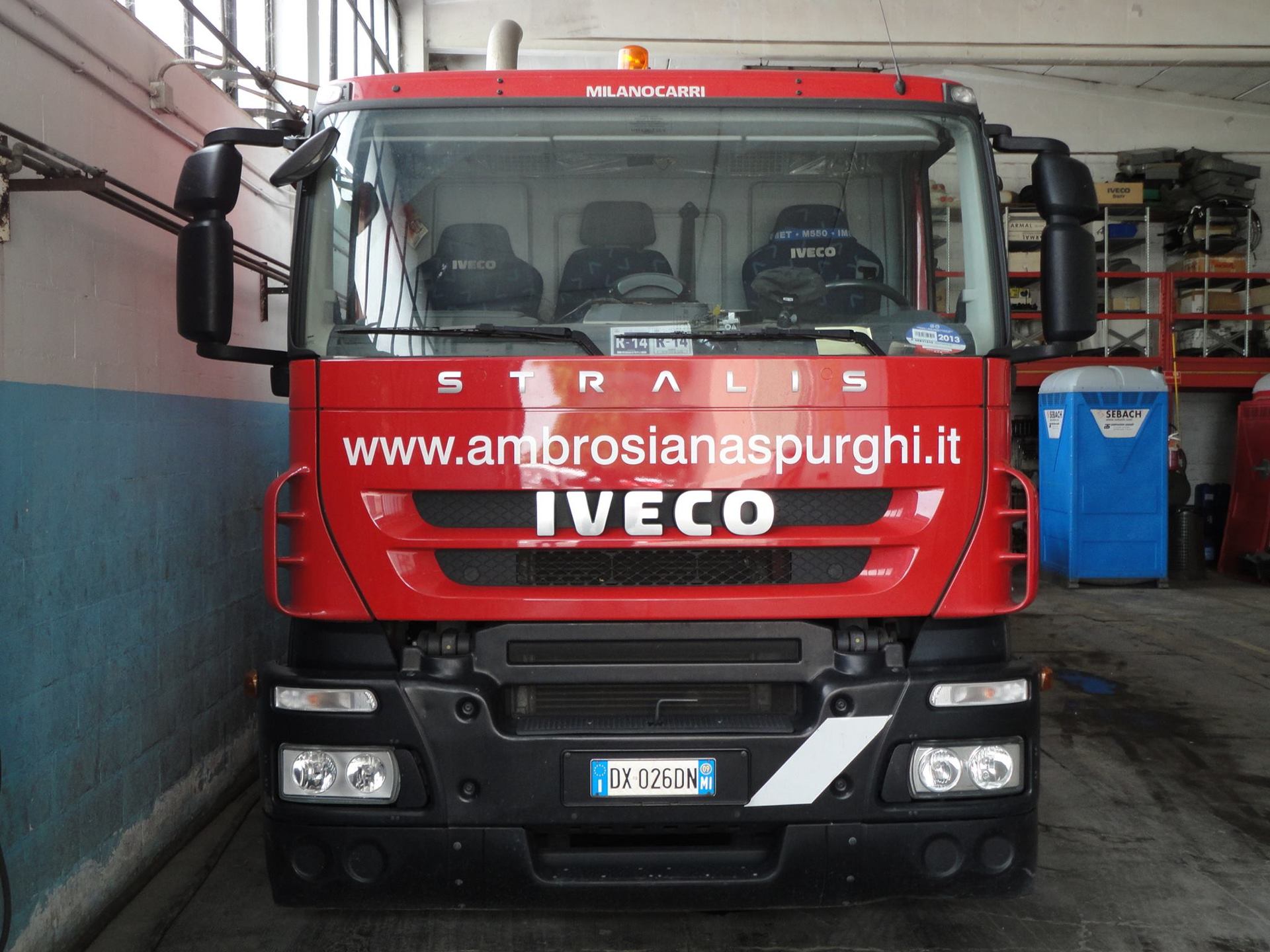 Camion IVECO Stralis rosso con logo e sito web, parcheggiato all'interno.