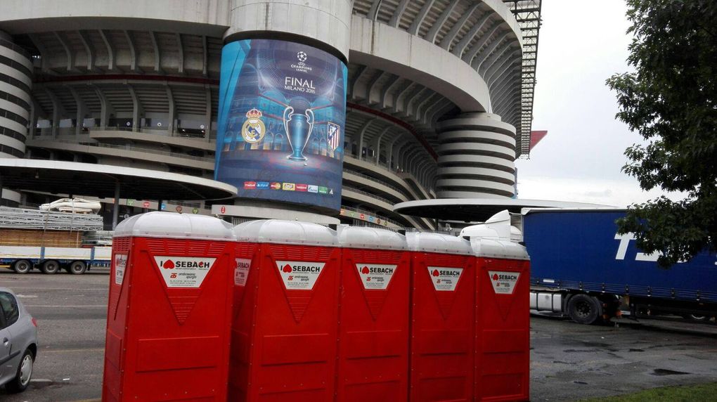 Bagni chimici rossi davanti a uno stadio con uno striscione della Champions League.
