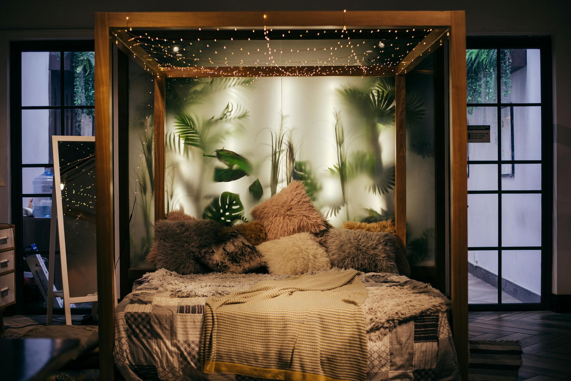 Four-poster bed with fairy lights, pillows, and leafy backdrop. Interior with a mirror and window.