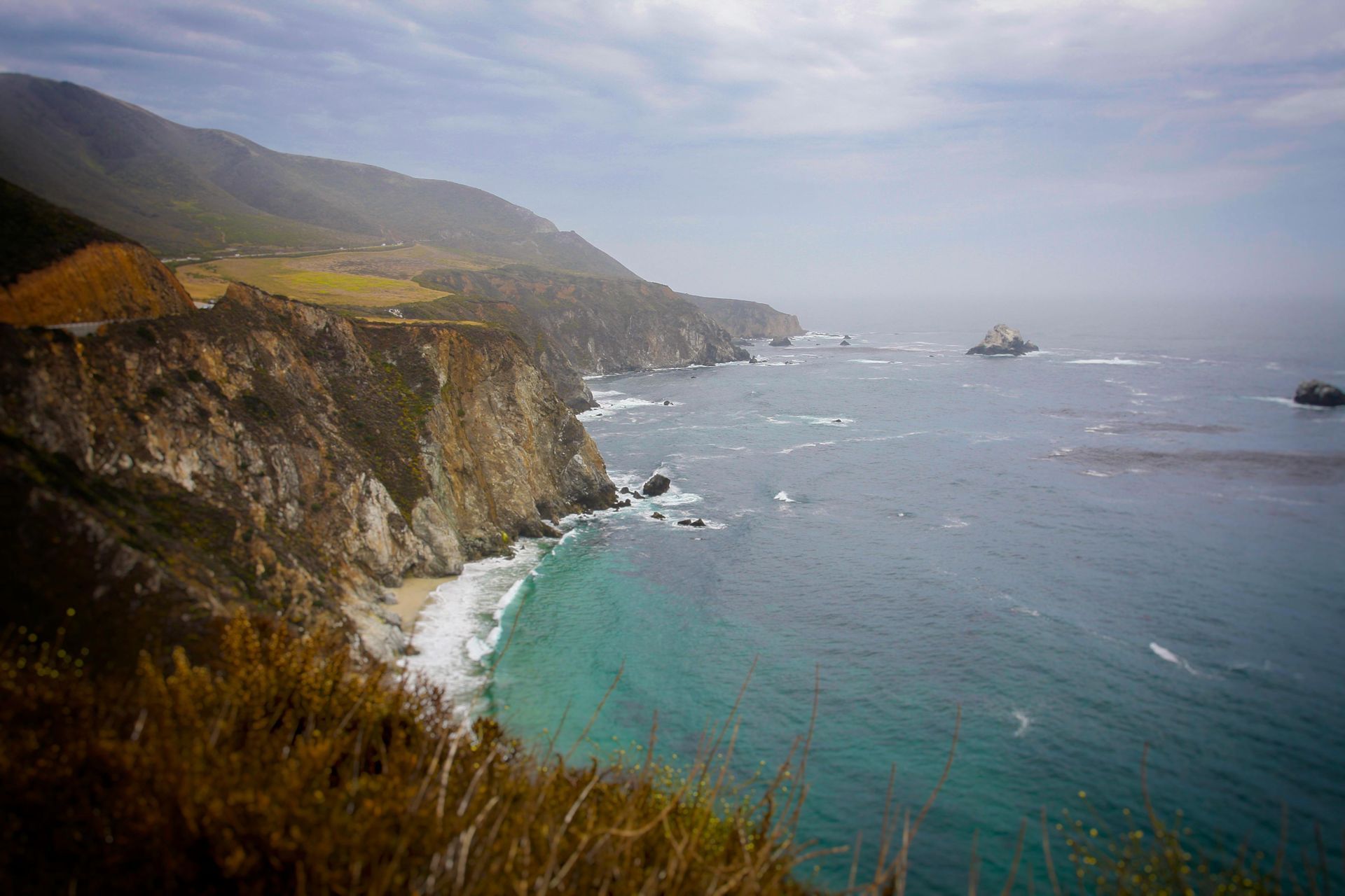 Coastal view: cliffs meet the ocean. Turquoise water, beige cliffs, and a cloudy sky.