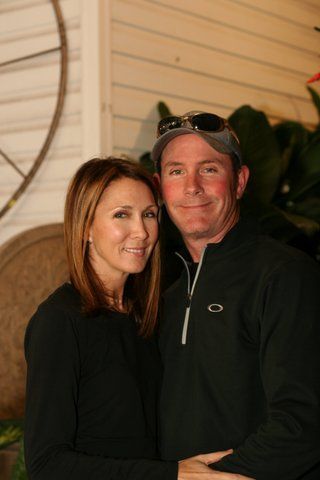 Couple posing; woman with long hair in black shirt, man in zip-up, sunglasses on cap.