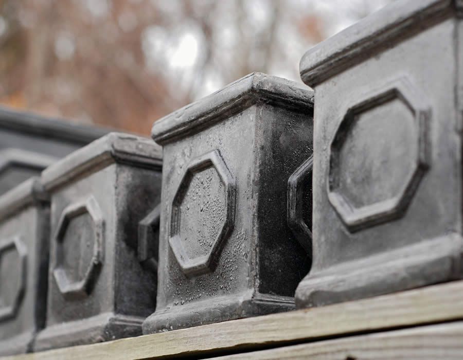 Close-up of a series of dark, decorative concrete posts with octagonal designs on a wooden structure. Close-up of a series of dark, decorative concrete posts with octagonal designs on a wooden structure.