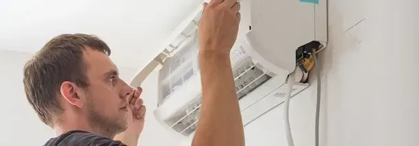Man is installing an air conditioner on a white wall.