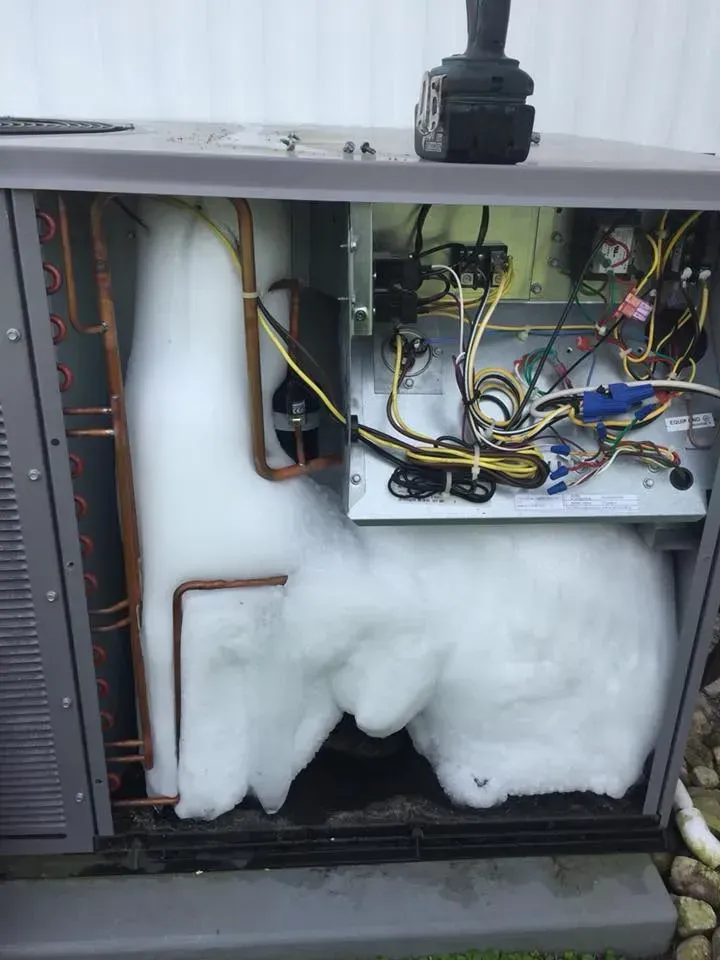 Outdoor HVAC unit with thick ice buildup inside, exposing components.