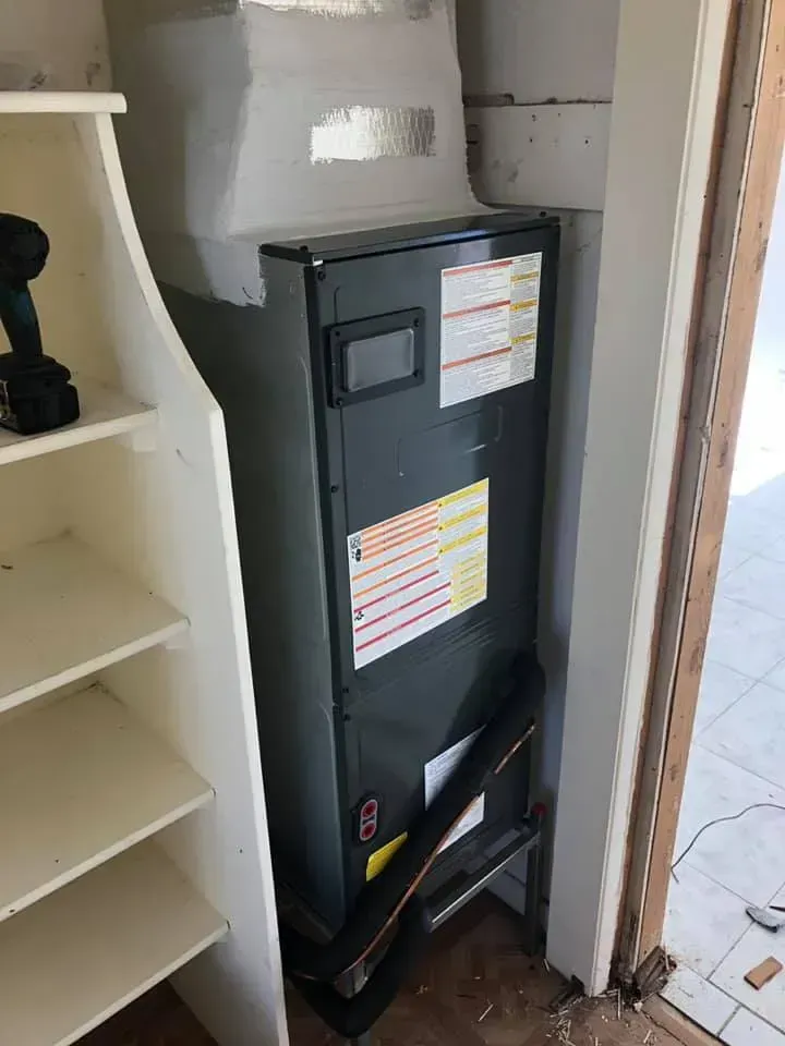 Furnace unit in a closet next to a shelving unit; a cordless drill sits on the shelf.
