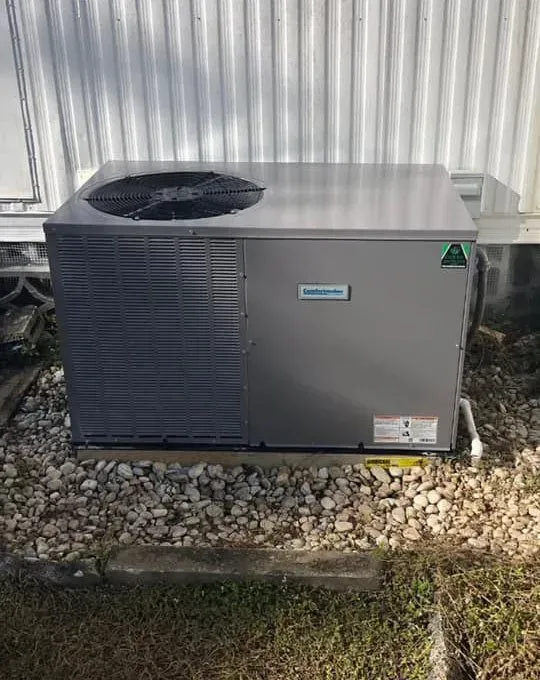 Gray air conditioner unit on gravel, next to a white-sided building.