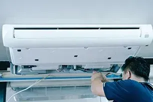 Person in blue shirt repairs an air conditioner attached to the ceiling.