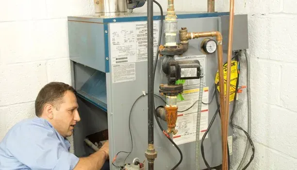 A man in a blue shirt working on a furnace in a utility room.