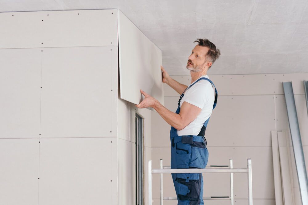 A man is standing on a ladder installing drywall on a wall — Mountain City Signs In West Tamworth, NSW