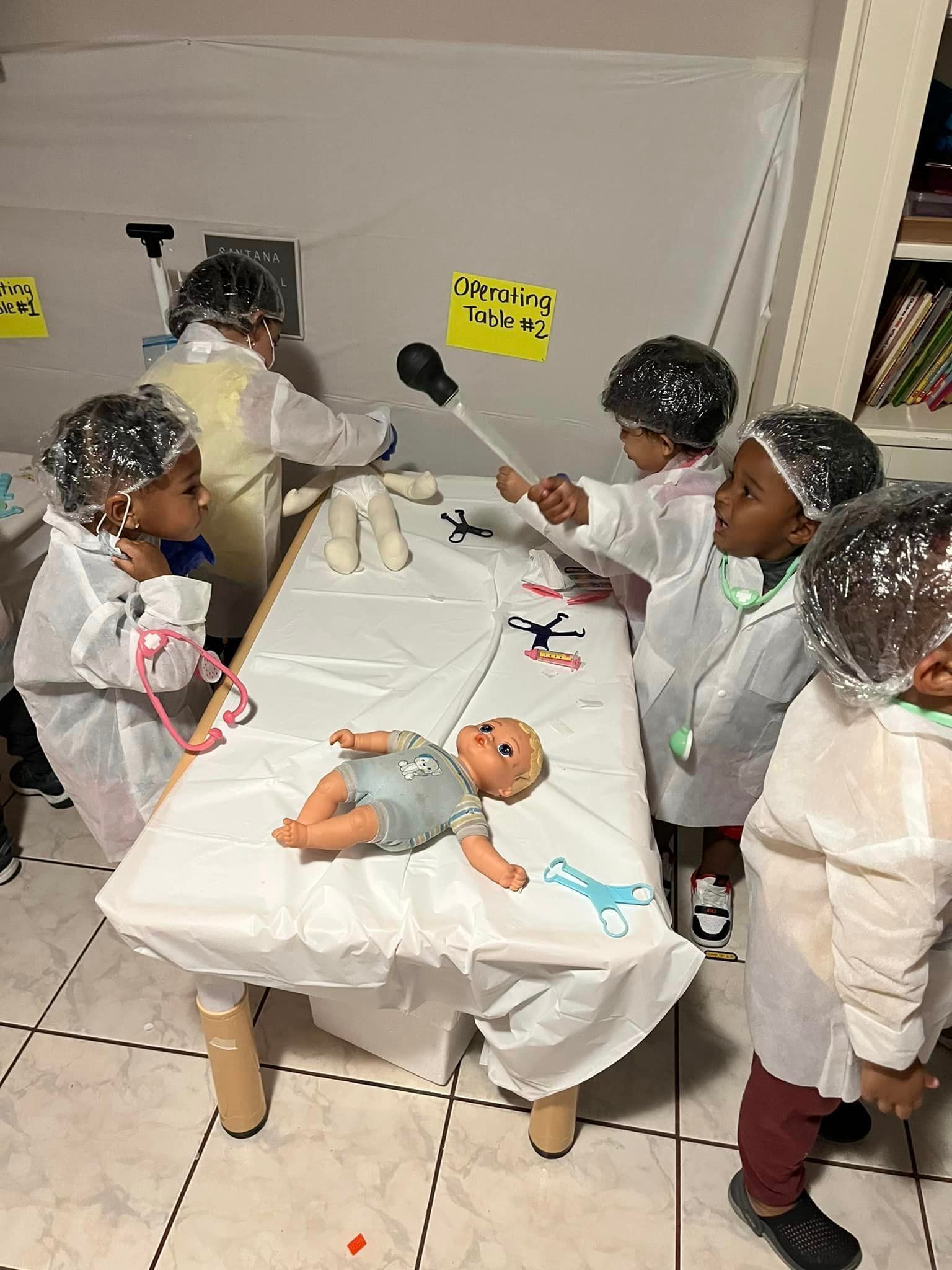 A group of children dressed as doctors are playing with a doll on a table.