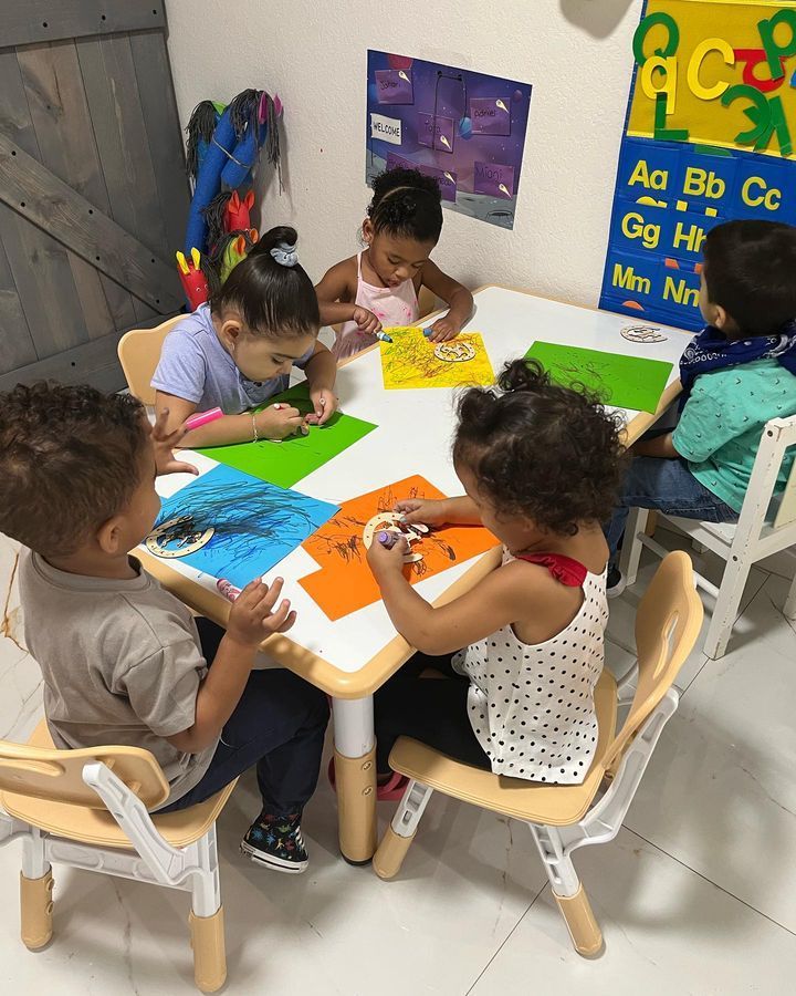A group of children are sitting at a table in front of a alphabet poster.