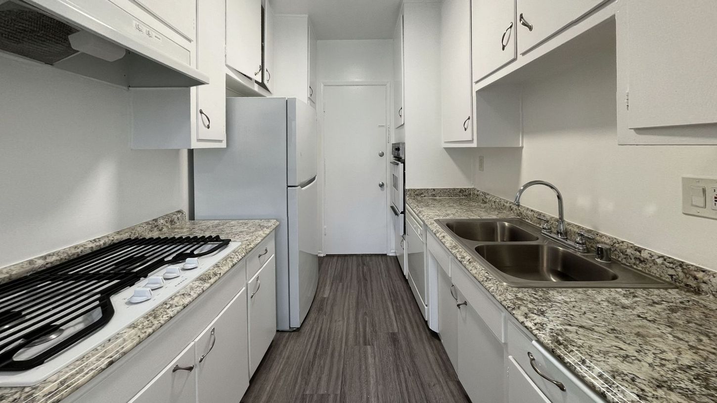 Narrow kitchen with white cabinets, granite countertops, and stainless steel sink and appliances.