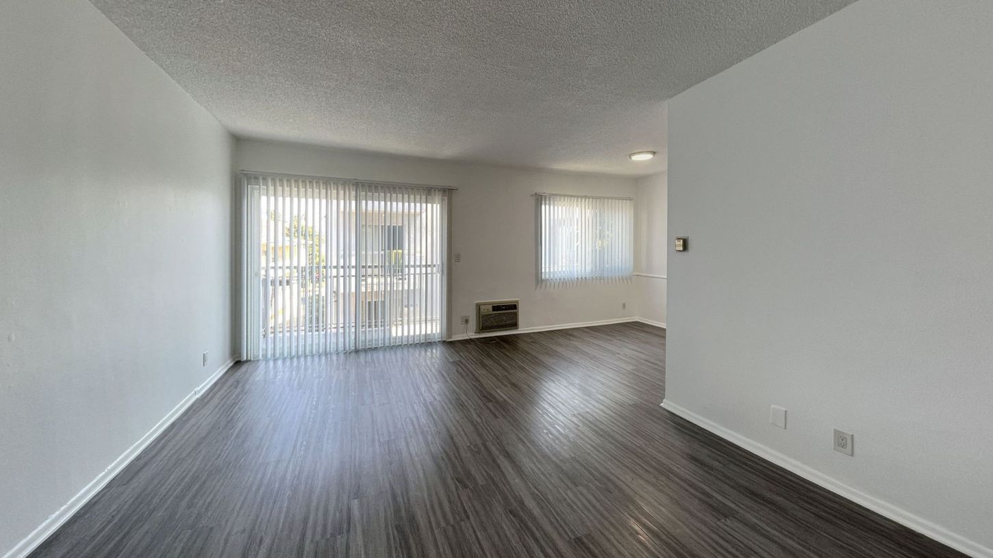 Empty living room with wood-look flooring, white walls, sliding glass door, and a window.
