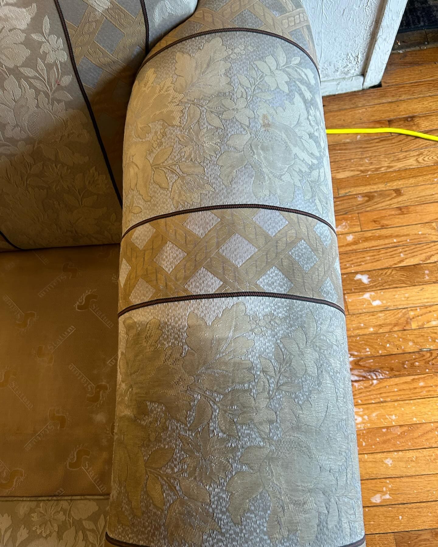 Close-up of a worn patterned upholstered couch armrest with frayed fabric seams.