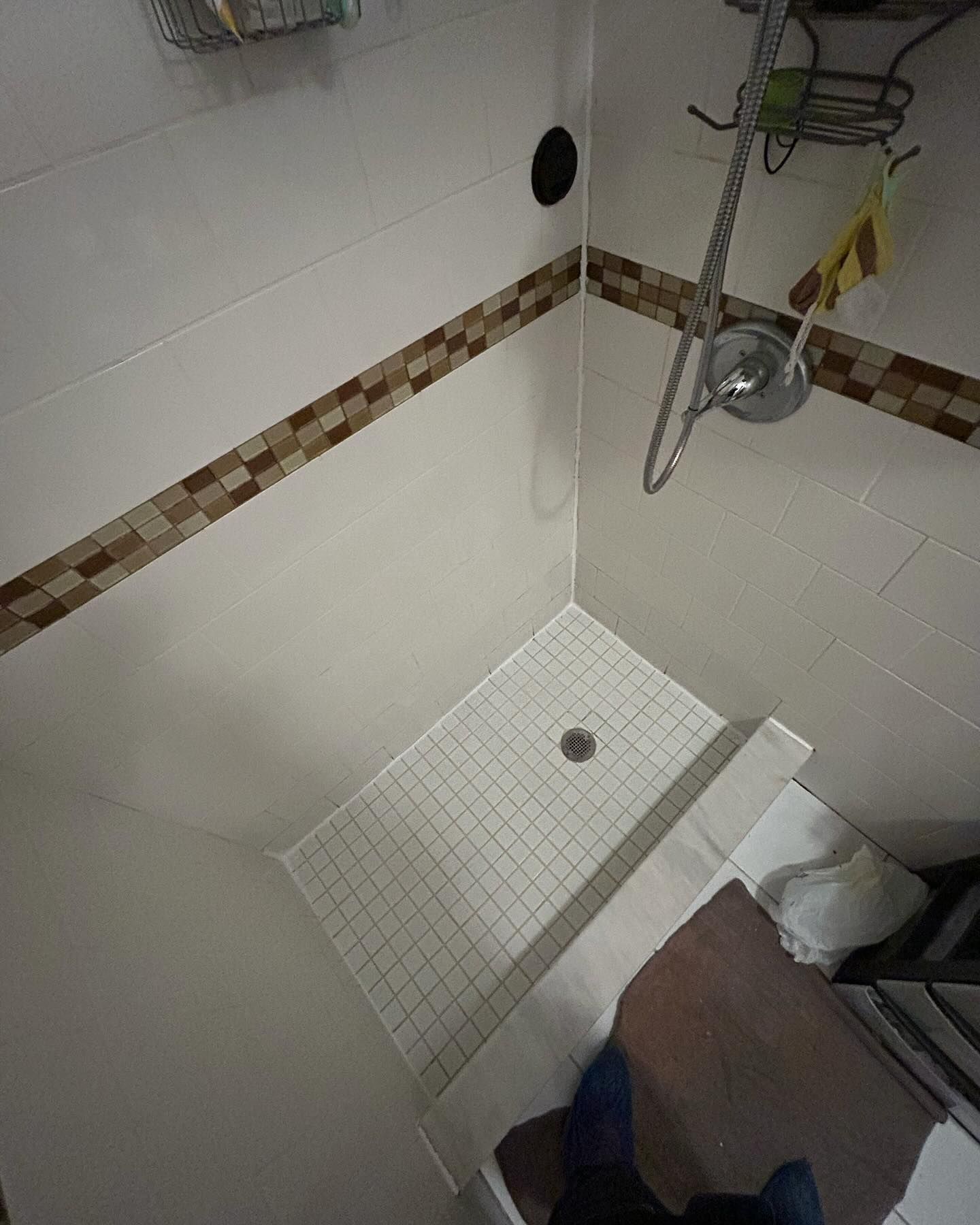 Small tiled shower stall with a white shower pan, handheld showerhead, and brown accent tile border.