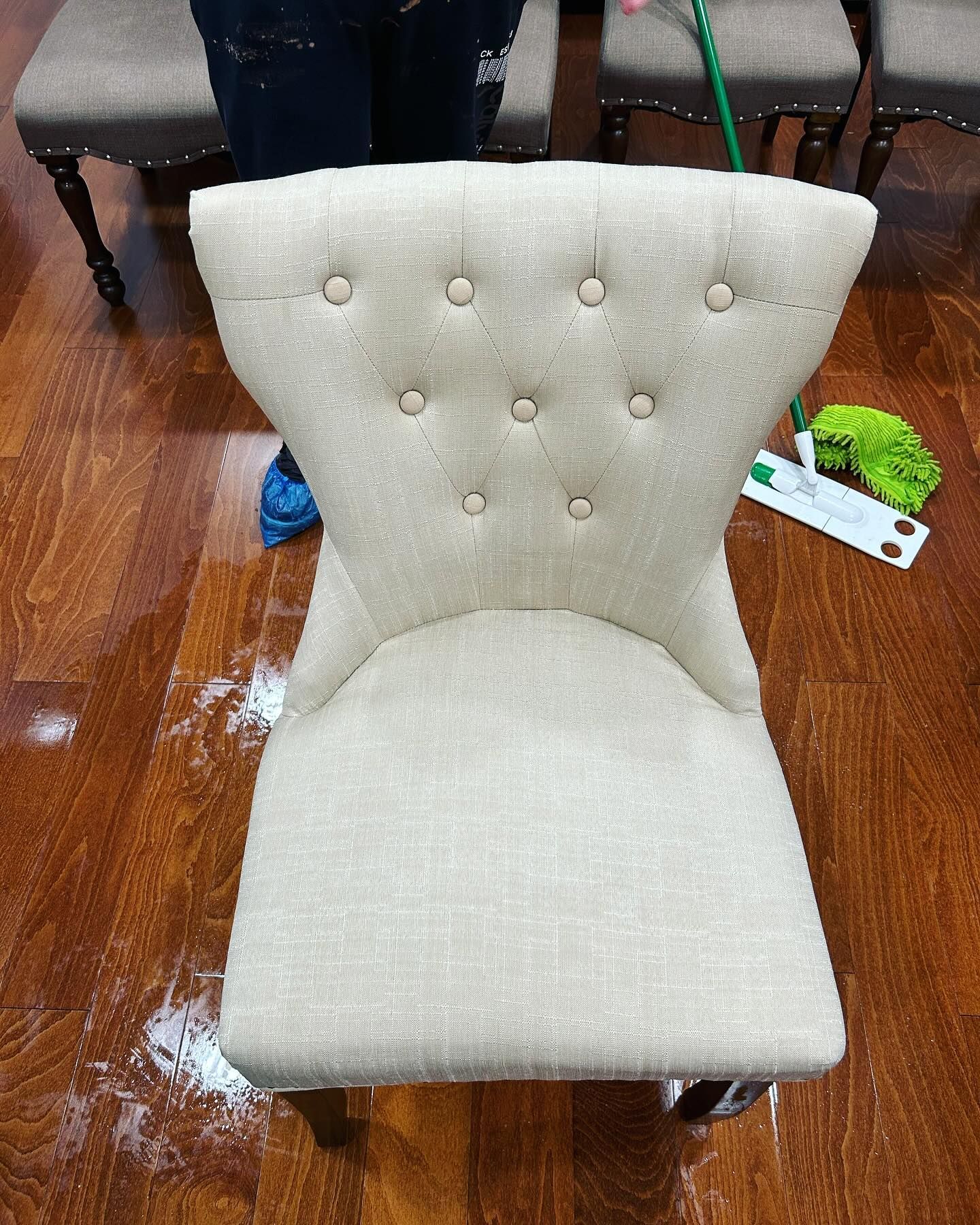 Beige tufted chair on hardwood floor, with a person and cleaning supplies partially visible behind it.