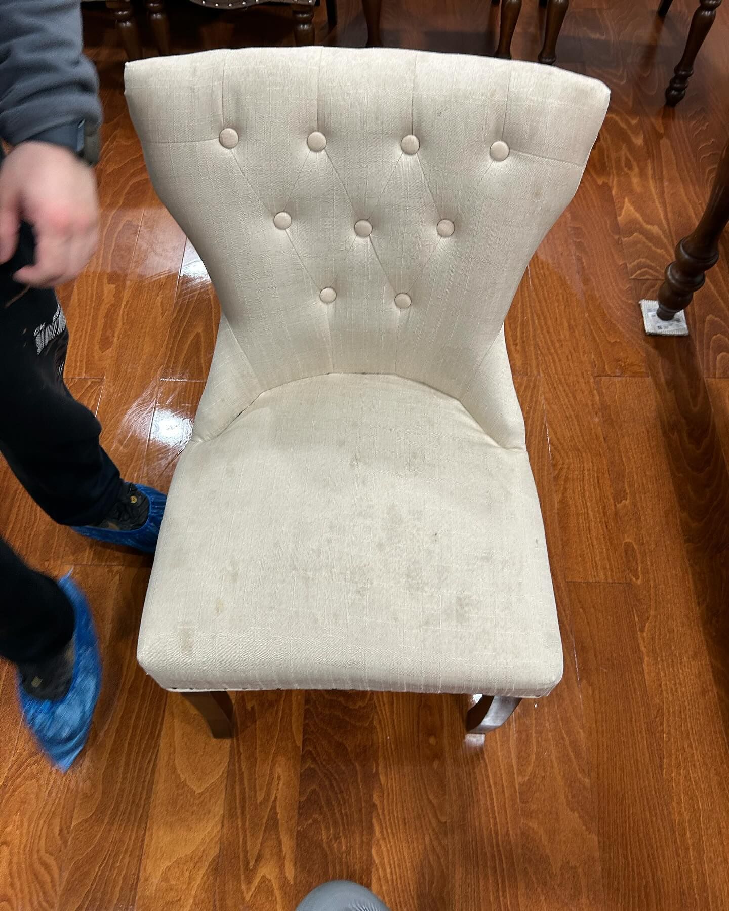 Beige tufted dining chair on a hardwood floor, with a person’s leg visible at left.