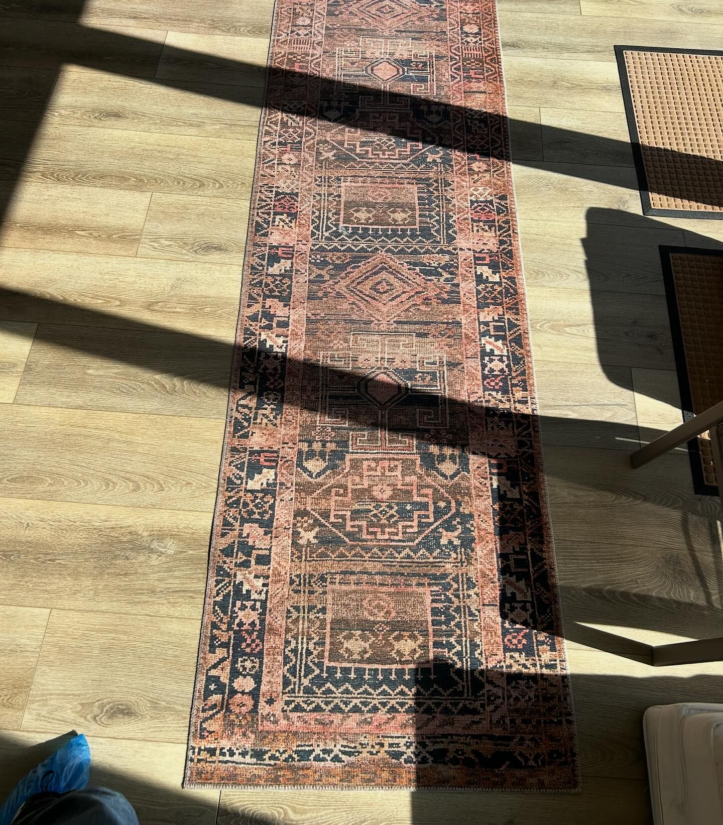 Long patterned runner rug on sunlit floor with chair shadows across it