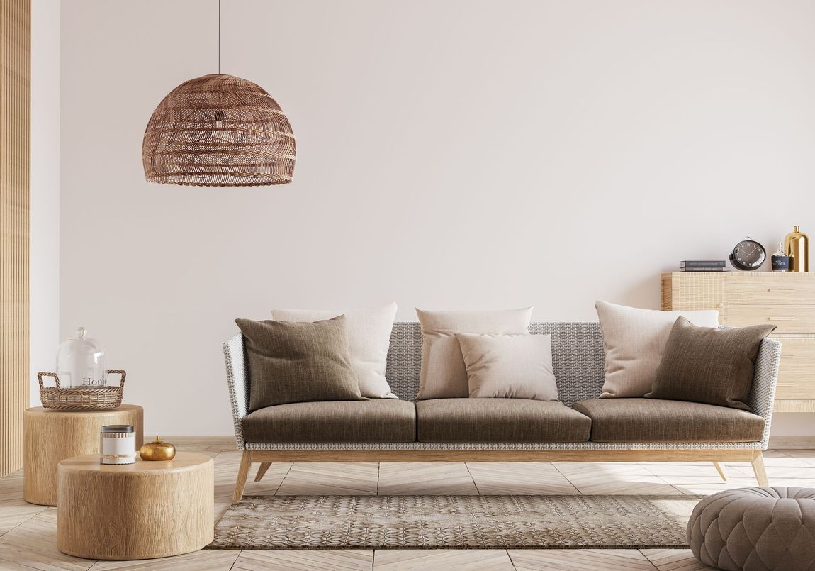 Minimalist beige living room with sofa, rug, woven pendant light, and wooden side tables.
