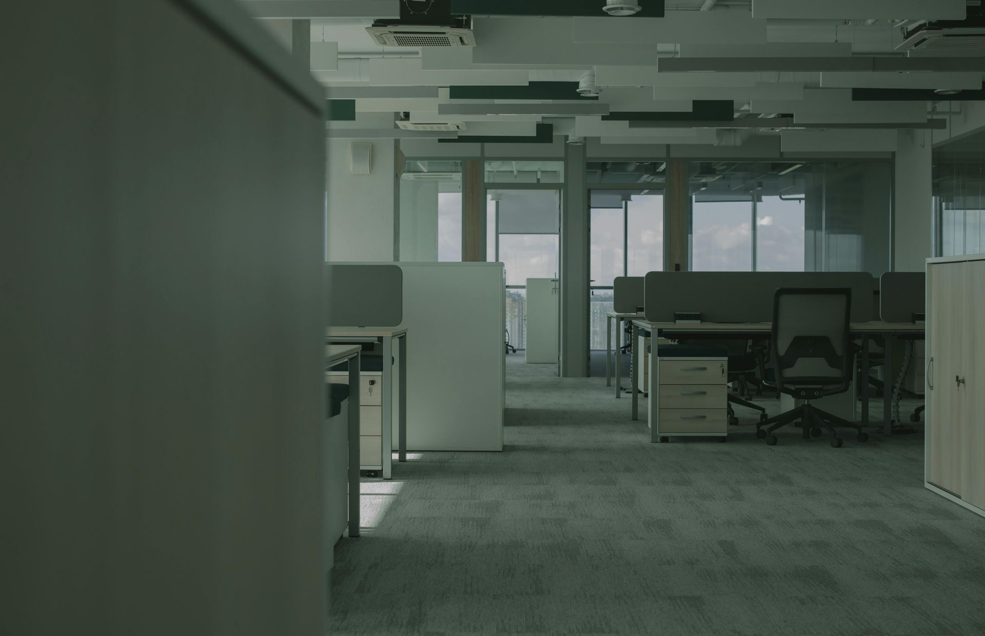 Empty office interior with desks, chairs, and large windows in muted green-gray light