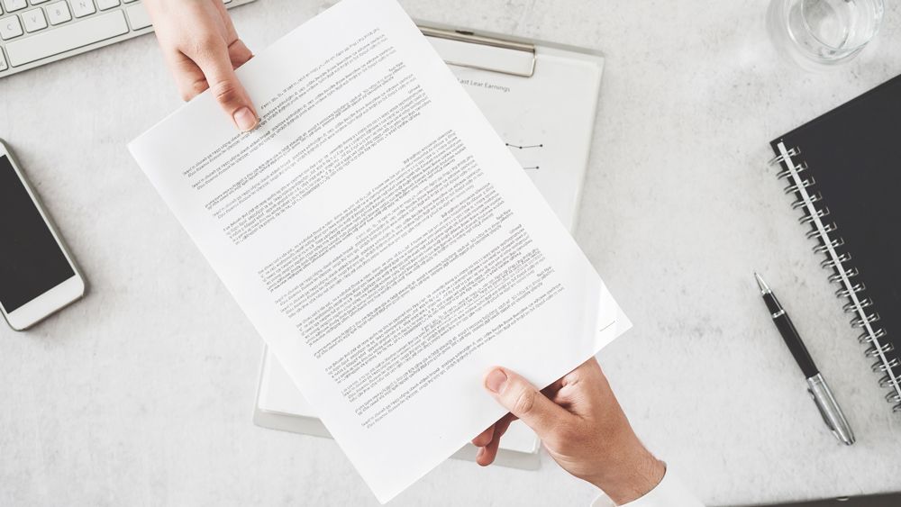 A person is holding a piece of paper in front of a desk