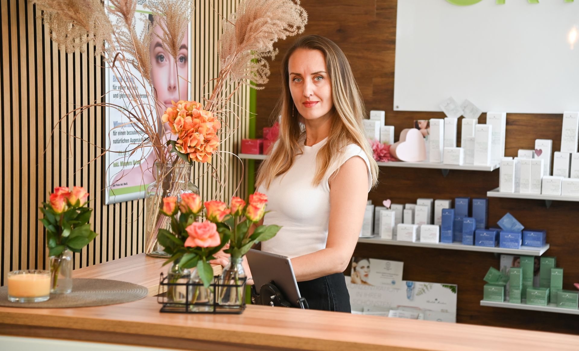 Eine Frau steht mit einem Tablet in der Hand an einem Tresen in einem Schönheitssalon.