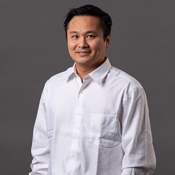Man in black shirt, looking at the camera, against a grey backdrop.