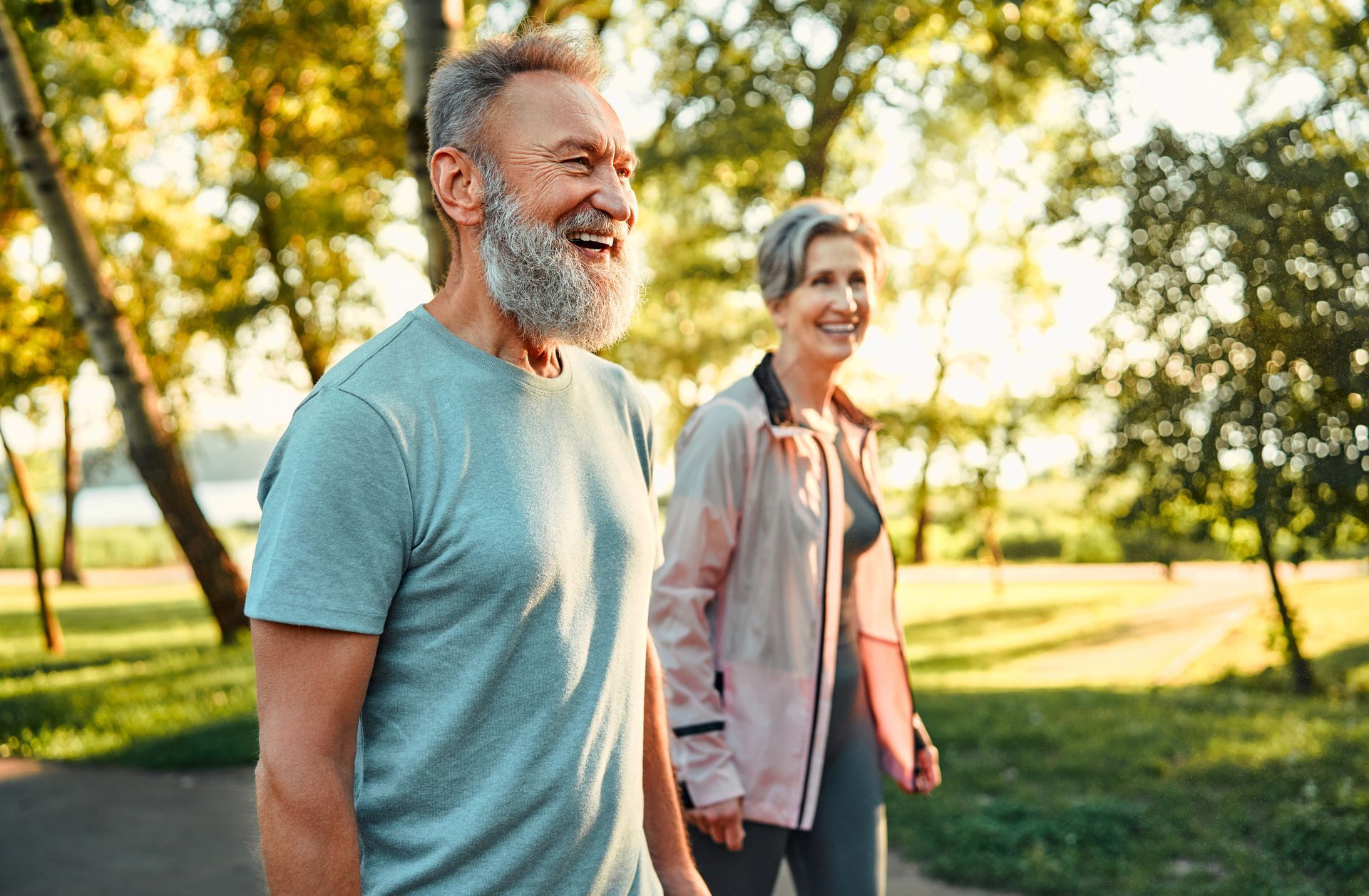 Older couple smiling while walking outdoors on a sunny day.