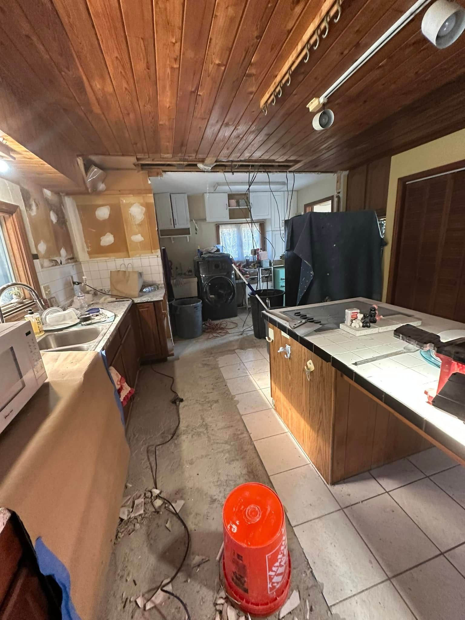 Kitchen under renovation, debris on floor, cabinets and ceiling exposed, red bucket.