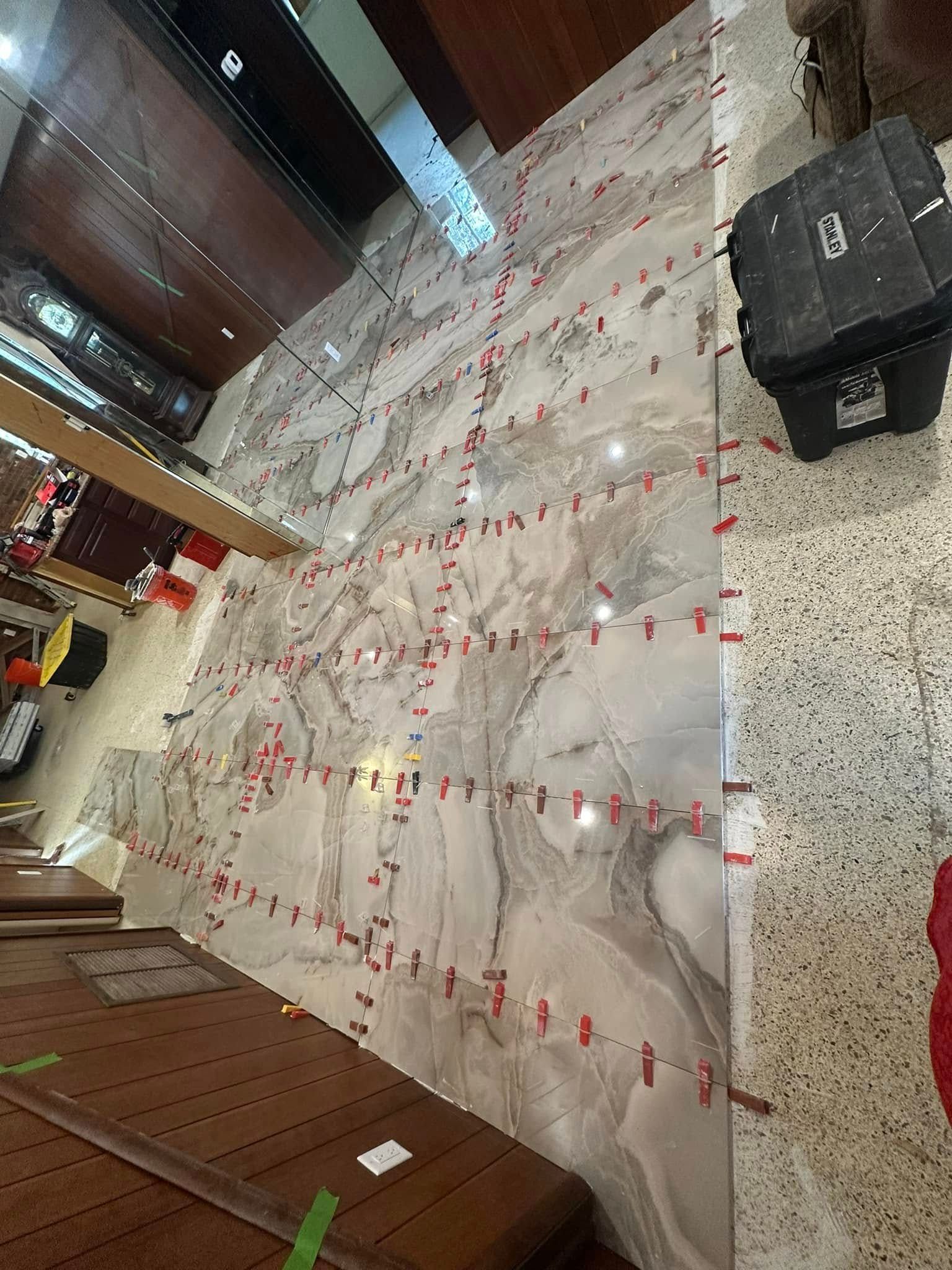 Large marble tiles being installed on a wall, with red leveling clips in use.