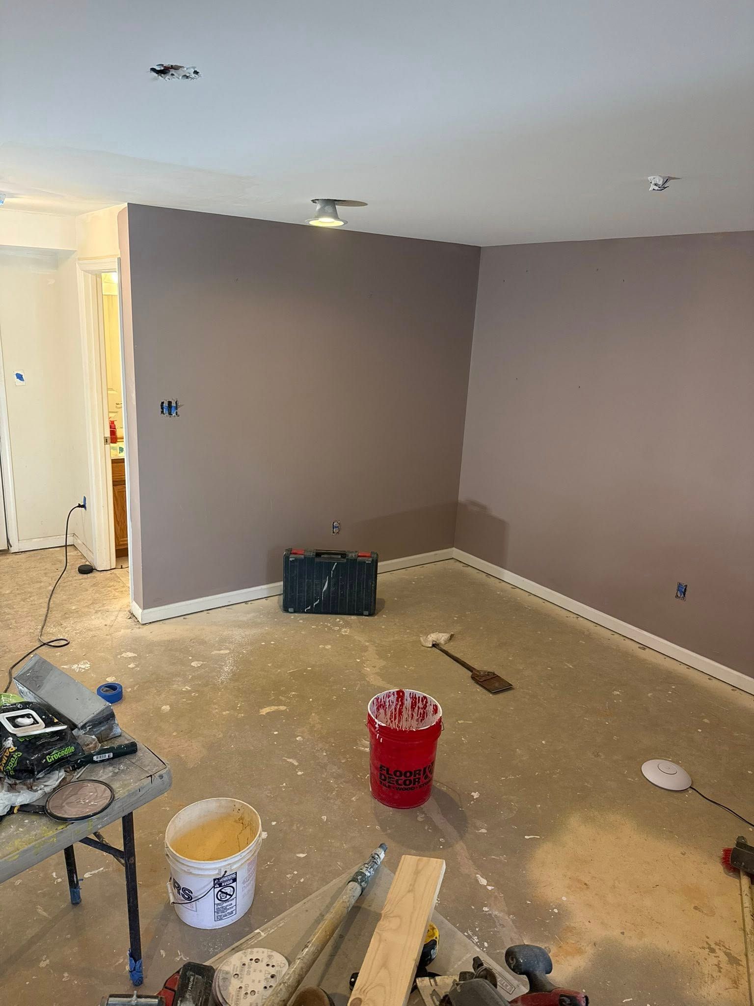 Room being renovated, with mauve walls, paint splatters on the floor, and painting supplies scattered about.