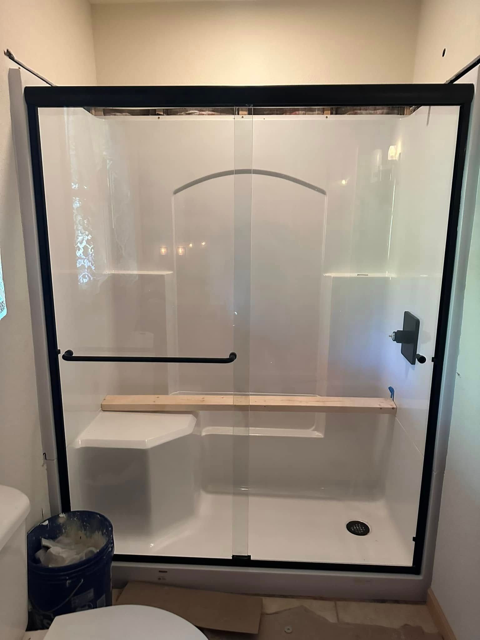 New shower enclosure with black frame, white walls, and a built-in seat.