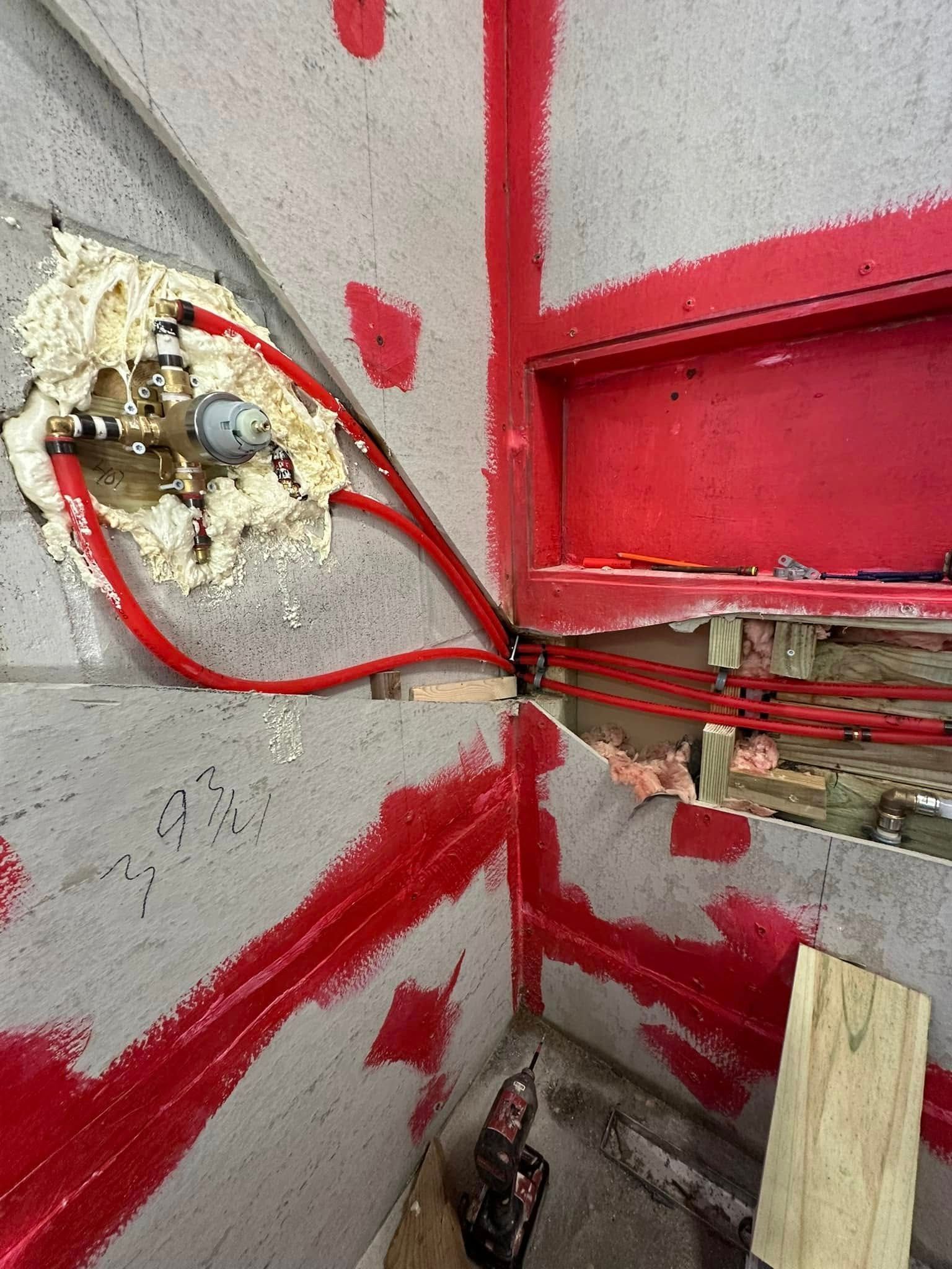 Plumbing in unfinished bathroom. Red pipes and trim, fixtures encased in foam, open wall, corner shelf.